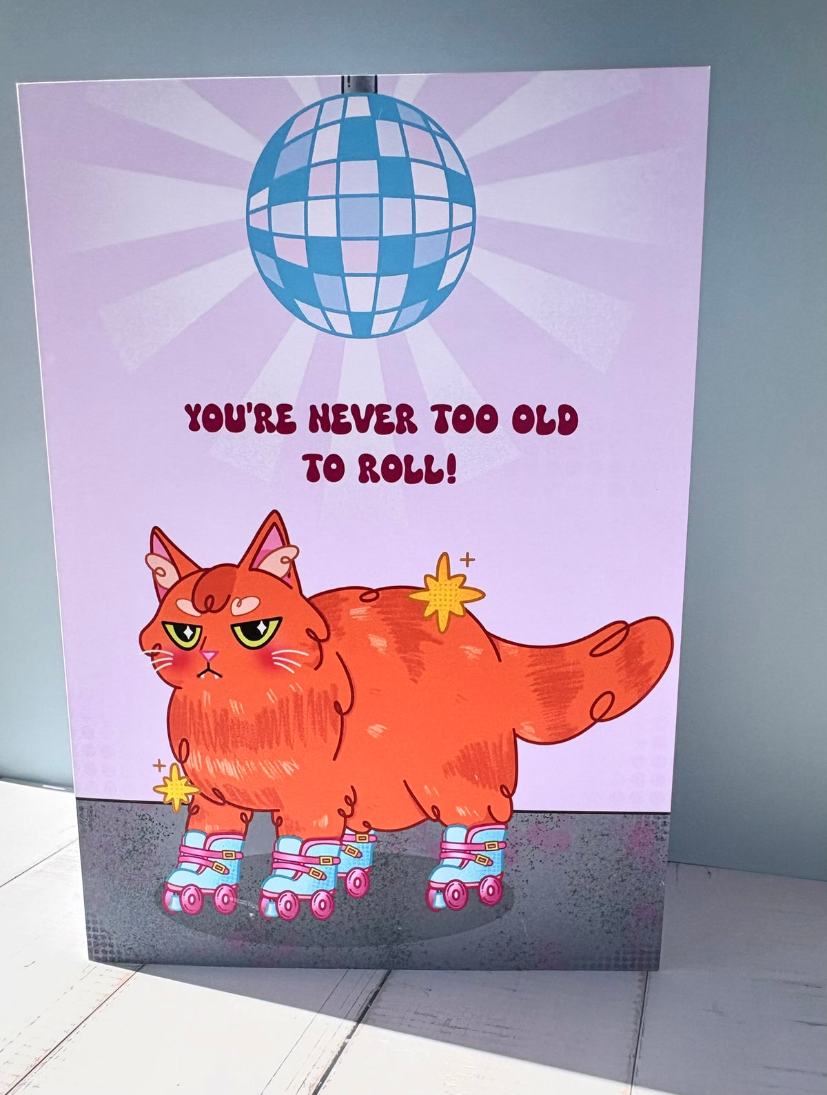 Roller Cat birthday card featuring a grumpy ginger cat on roller skates under a disco ball