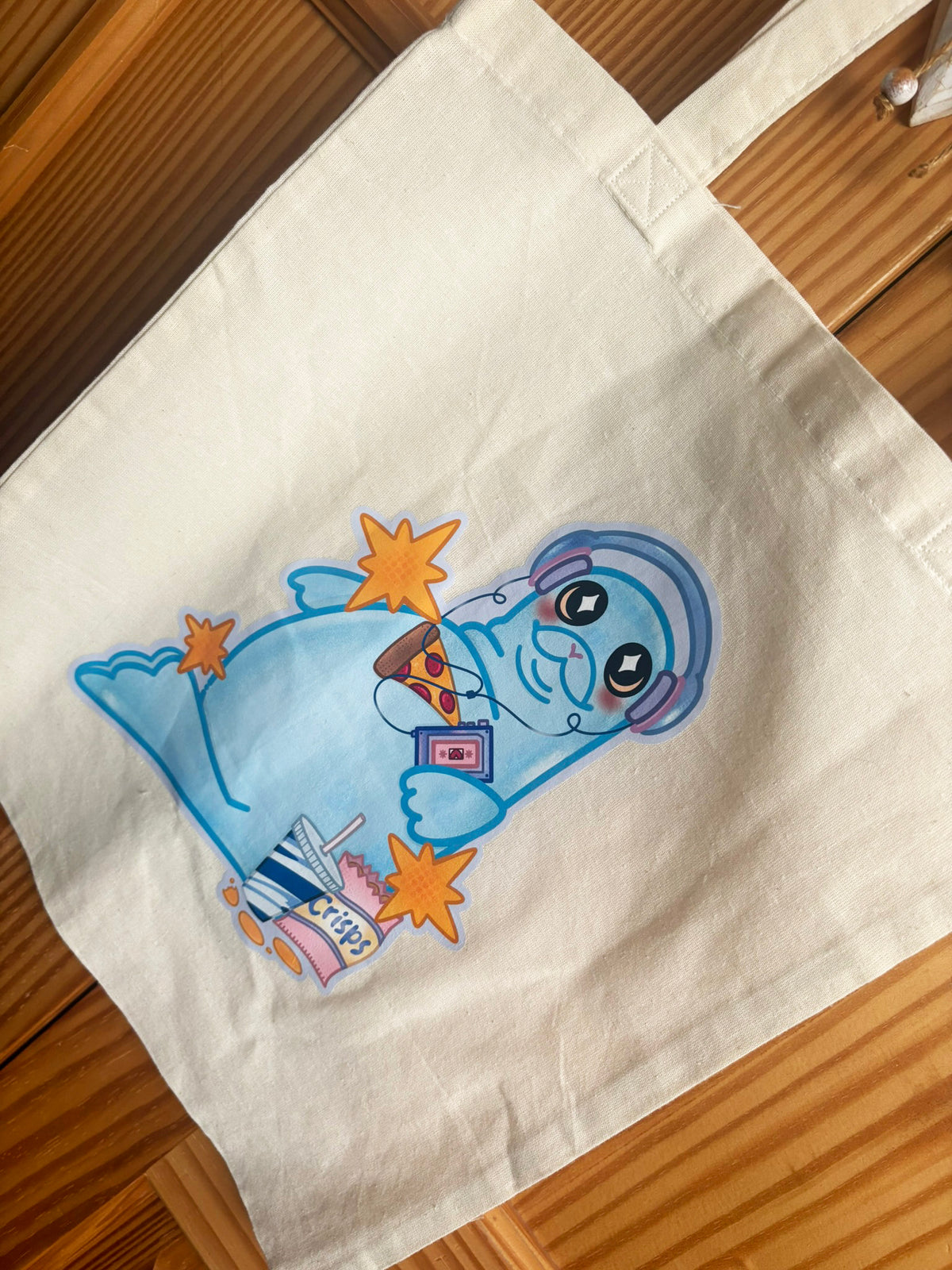Close-up of Snack Seal tote illustration with pizza, crisps, a drink and orange stars