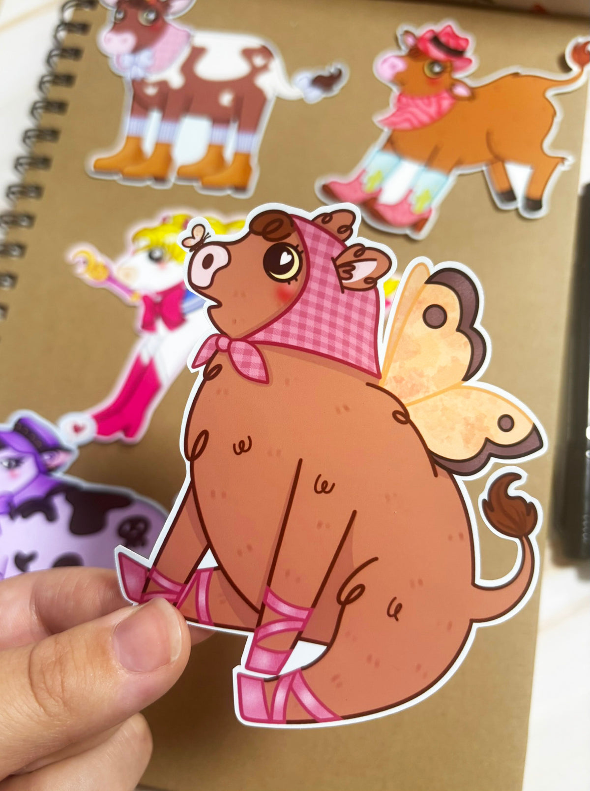 Brown cow sticker with yellow fairy wings, a pink gingham headscarf and pink ballerina shoes.