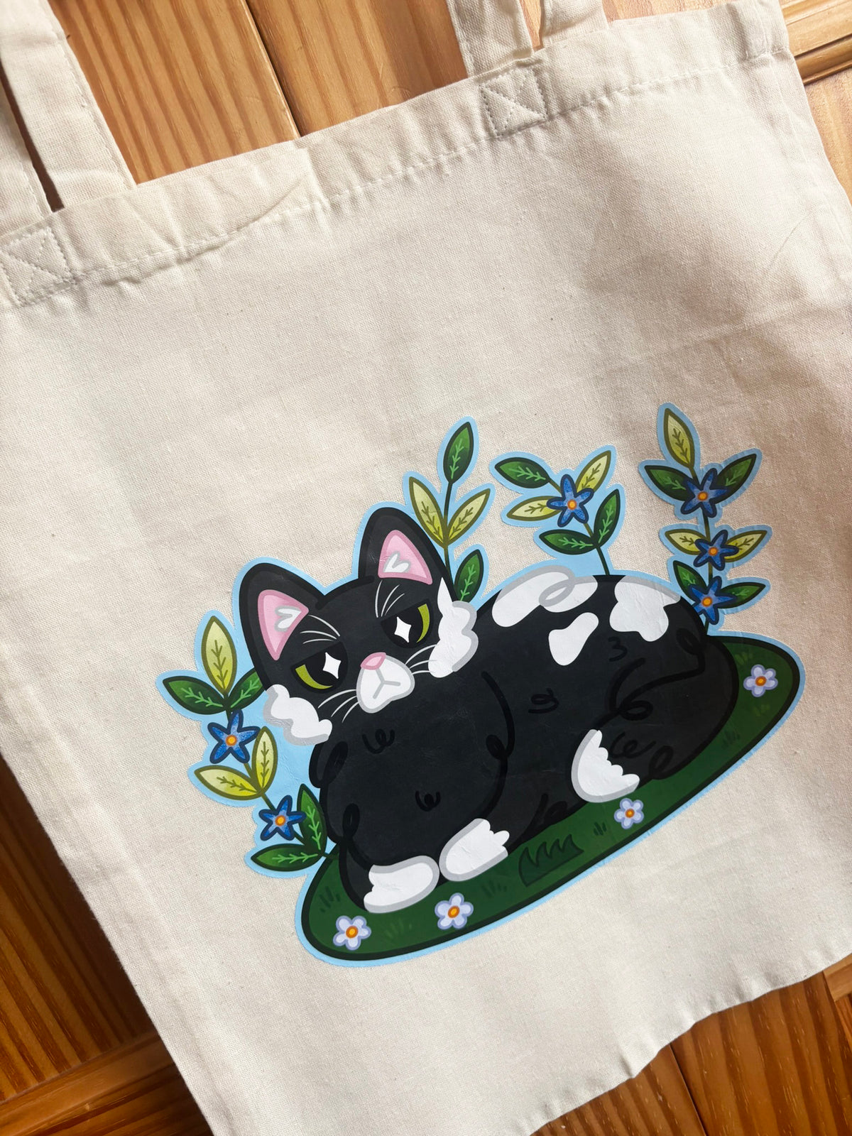 Close-up of the Garden Cat tote bag illustration with green leaves and blue flowers