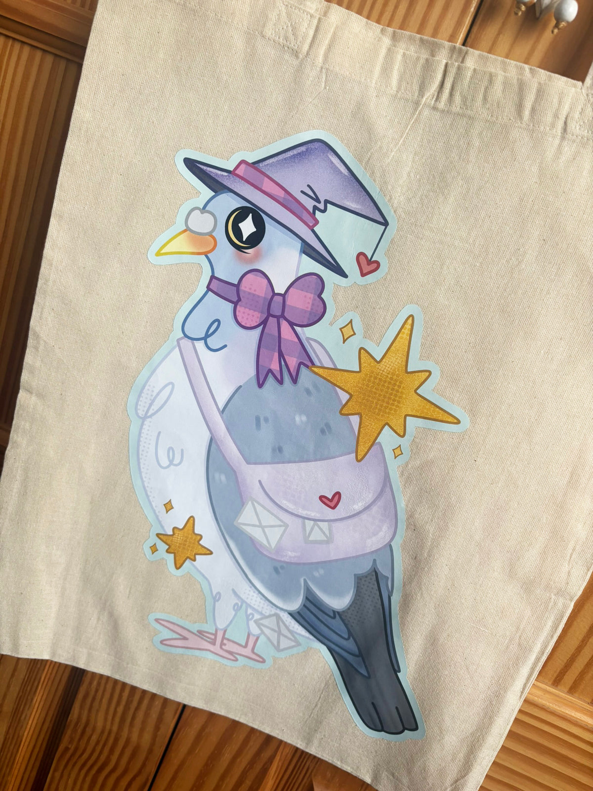 Close-up of witch carrier pigeon illustration with purple bow, lilac satchel and golden stars